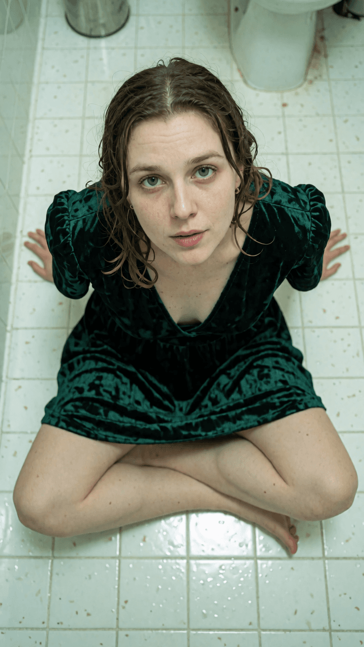 Woman in a deep emerald green velvet dress sitting on a tiled bathroom floor